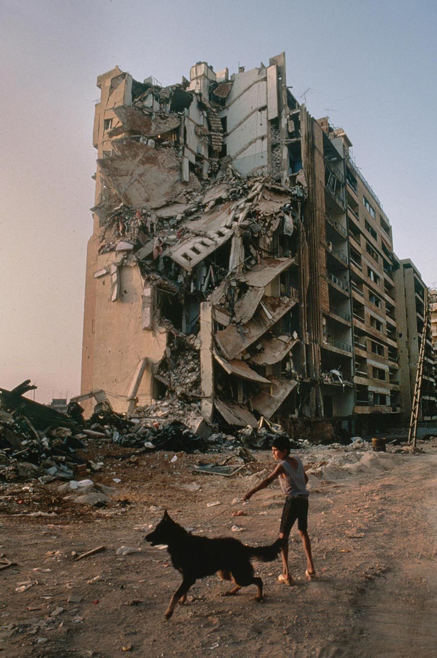A boy walking a dog beside a damaged building